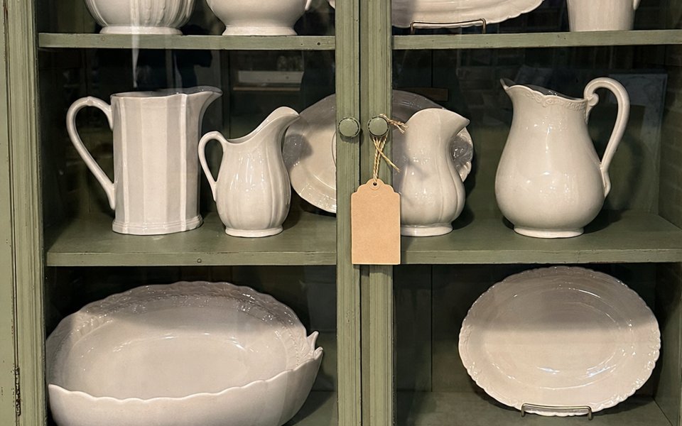 Shelves of white ironstone pitchers in a sage-green hutch